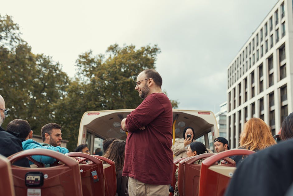 Group of people enjoying scenic open-top bus ride in an urban setting on a cloudy day.